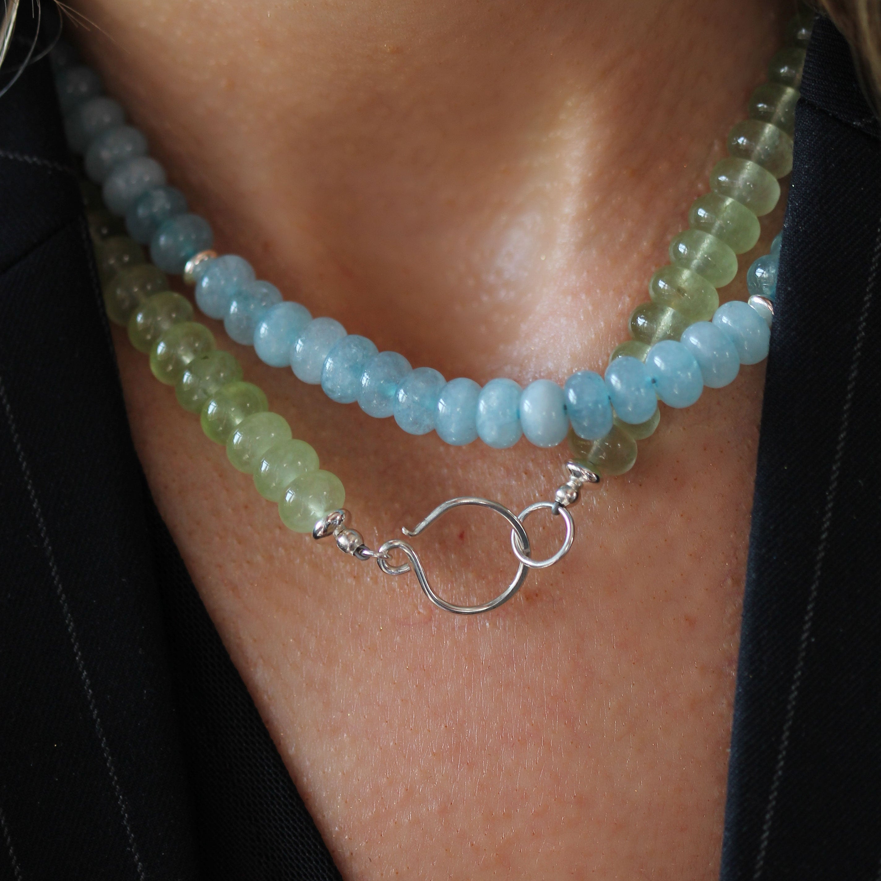 A close-up of a person wearing a double-strand beaded necklace with light blue and pale green beads and a silver clasp, paired with a black top.