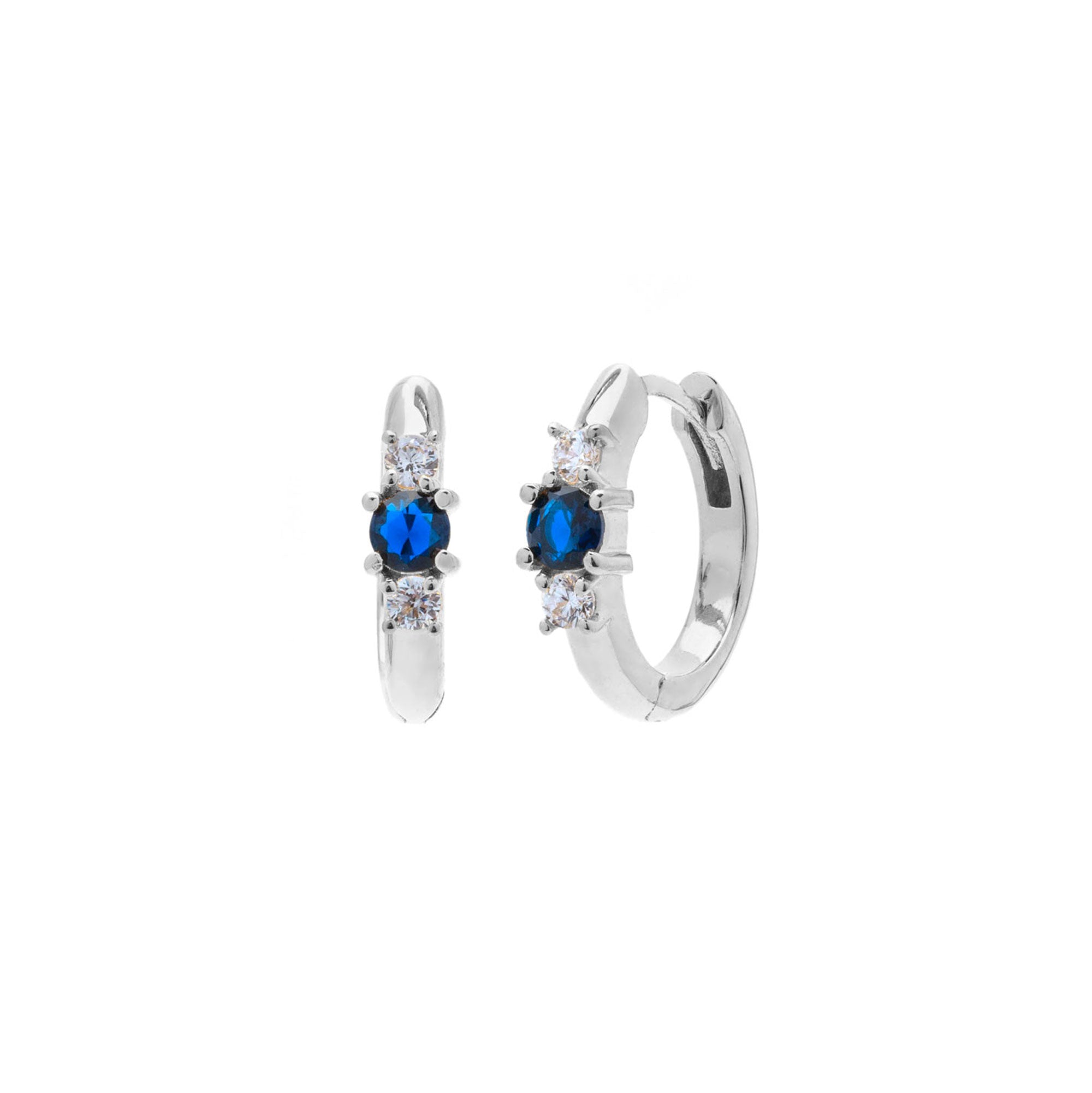 A pair of silver huggie hoop earrings featuring a central round blue gemstone flanked by small clear cubic zirconia stones, shown on a plain white background.
