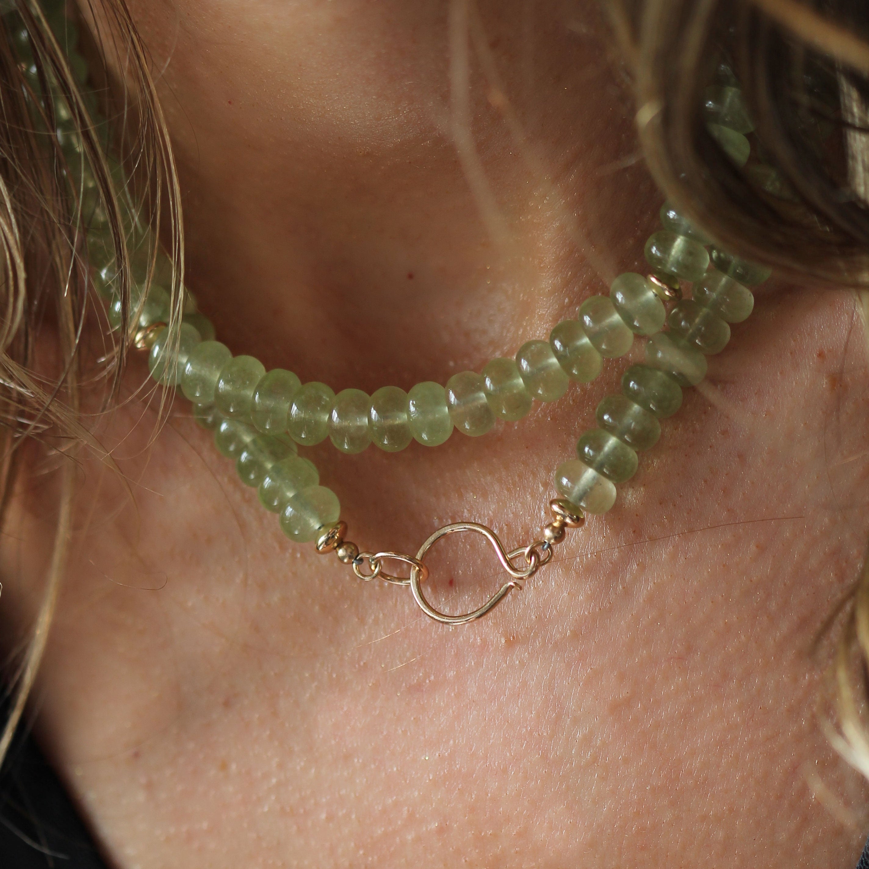A close-up of a person wearing a double-strand beaded necklace made of translucent light green beads with a gold-tone open ring clasp.